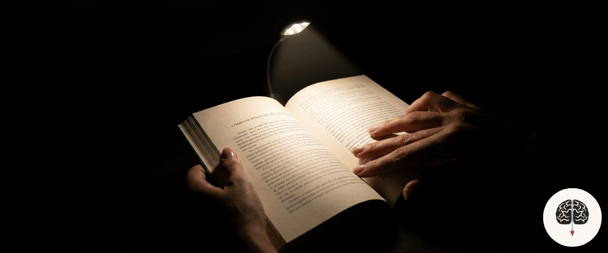 Pessoa lendo livro com luz de clipe LED em ambiente escuro